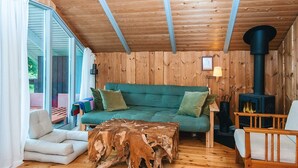 A cozy cabin interior with a wooden ceiling, a green sofa, a wooden coffee table, and a wood-burning stove. - 5 Person Holiday Home in Knebel (Knebel)