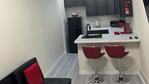 A compact kitchen with a black refrigerator, a microwave, and a red coffee machine. There are two red bar stools and a black sofa with red cushions. - 1,2,3,4 Escape comfort & style. You'll love it!" (Las Vegas)