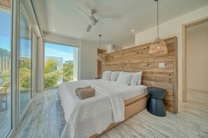 A modern bedroom with a large bed, a ceiling fan, and a view of the outdoors.