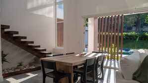 Ein modernes Interieur mit einer Holztreppe, einer Essecke mit Holztisch und -stühlen sowie Blick auf einen Garten und Pool.