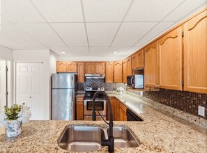 A kitchen with granite countertops, stainless steel appliances, wooden cabinets, and a backsplash.