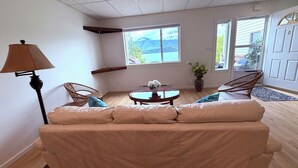 Ein Wohnzimmer mit einer Couch, einer Lampe, einem Tisch mit Blumen und Blick auf Berge durch die Fenster.