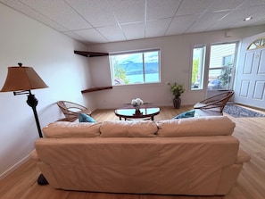 A living room with a sofa, a lamp, a table with flowers, and a view of mountains through the windows.