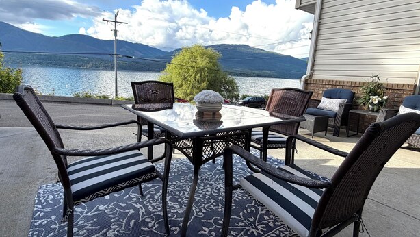 Eine Terrassenanlage im Freien mit Tisch, Stühlen, einem Teppich und Blick auf einen See und Berge.