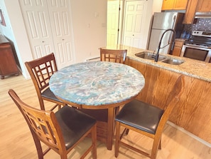A kitchen with a round table, wooden chairs, a stainless steel sink, and a refrigerator.