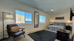 Une chambre à coucher comprenant un lit, une chaise, un bureau, une commode, un miroir et deux fenêtres.