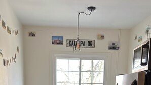 Une cuisine avec un sol en pierre, deux tabourets de bar, un réfrigérateur et une fenêtre donnant sur des arbres.