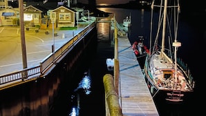 A dock with a sailboat moored at the pier, a small building with a sign, and a calm body of water reflecting the moonlight.