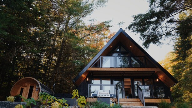 A modern cabin with a wooden exterior, large windows, and a covered porch area. - A-Frame retreat with hot tub, sauna (Huntsville)