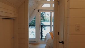 A narrow hallway with wooden floors and white walls leading to a bedroom with a bed and a window. - A-Frame retreat with hot tub, sauna (Huntsville)