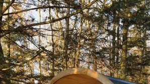 A wooden cylindrical cabin with a bench and a table inside, surrounded by trees. - A-Frame retreat with hot tub, sauna (Huntsville)