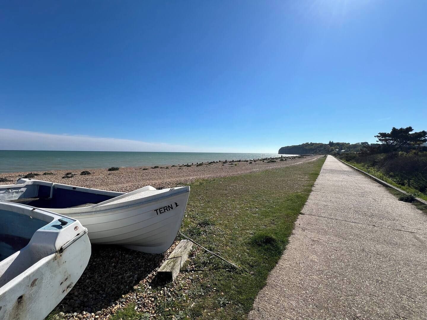Una playa de guijarros con una hilera de barcos y un sendero pavimentado.
