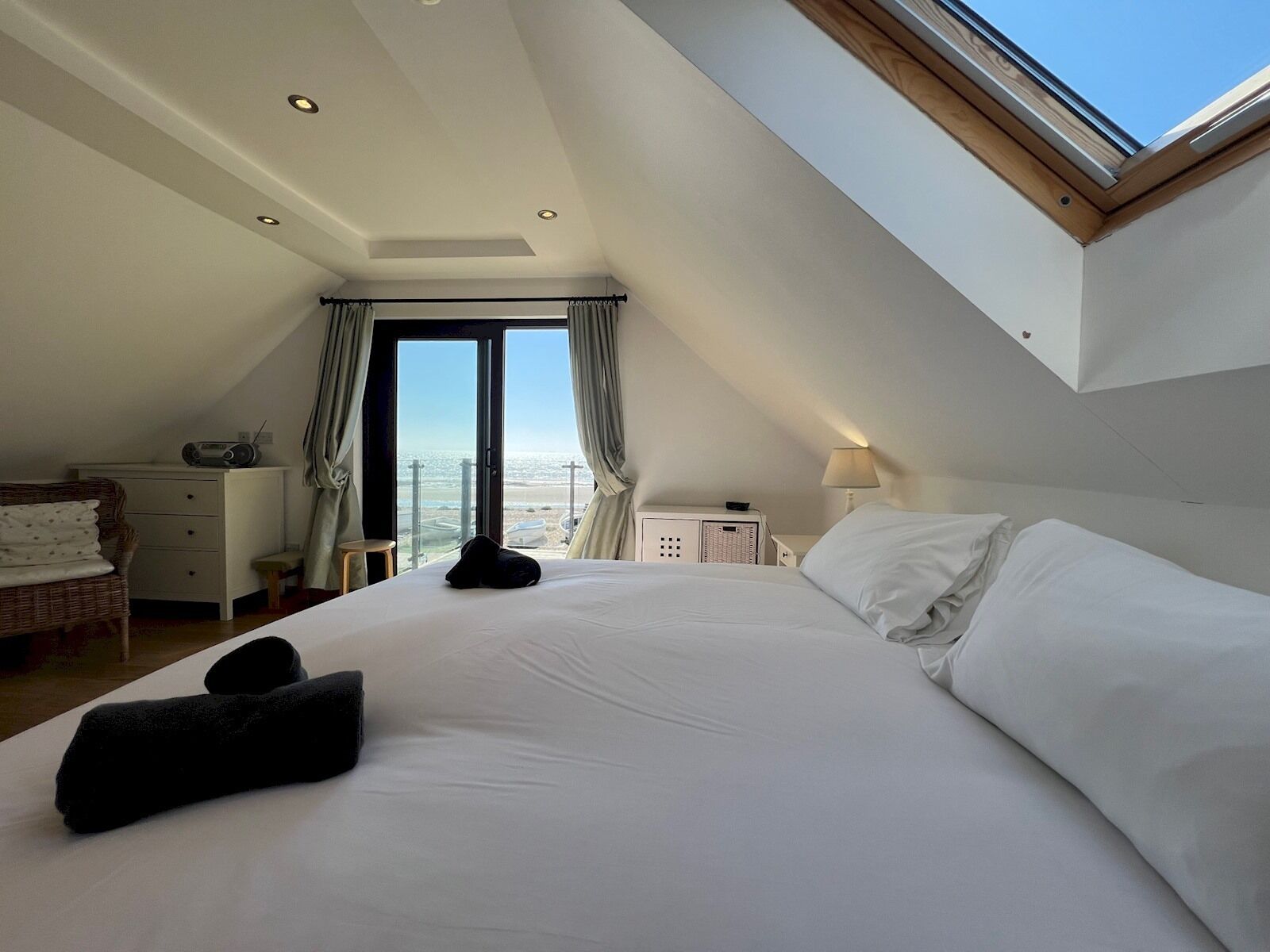 A hotel room with a large bed, a desk, a chair, and a view of the sea through a large window.