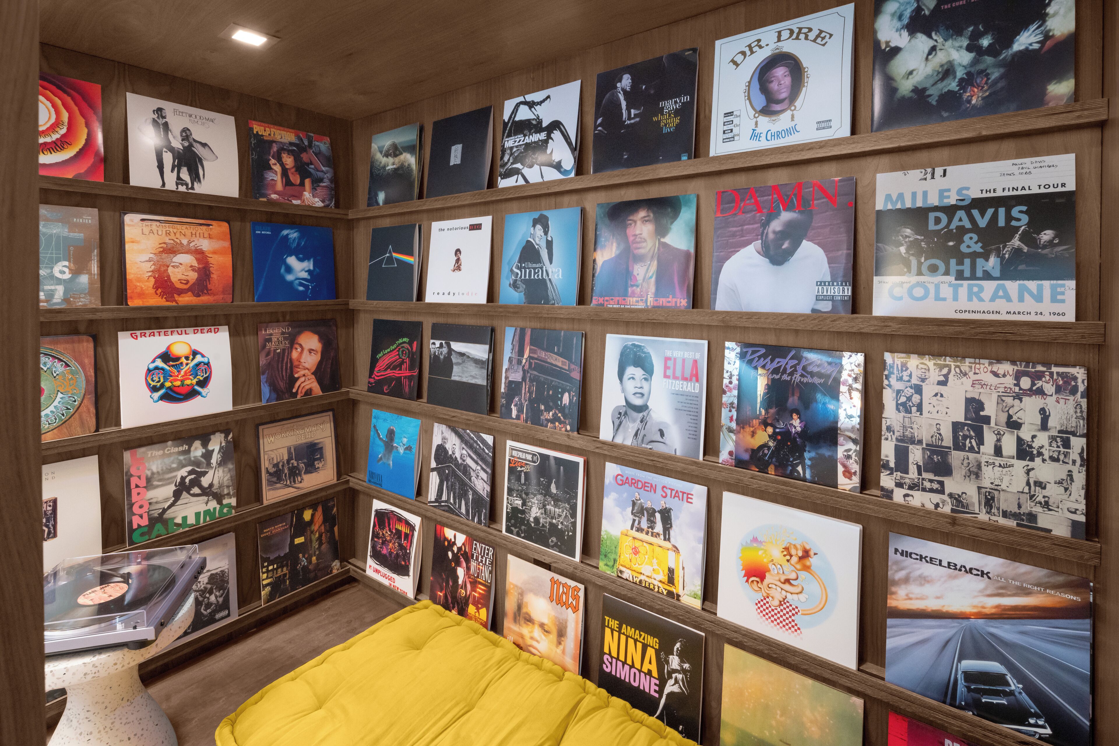 Una habitación con una cama, un estante con portadas de discos y una mesita con un tocadiscos.