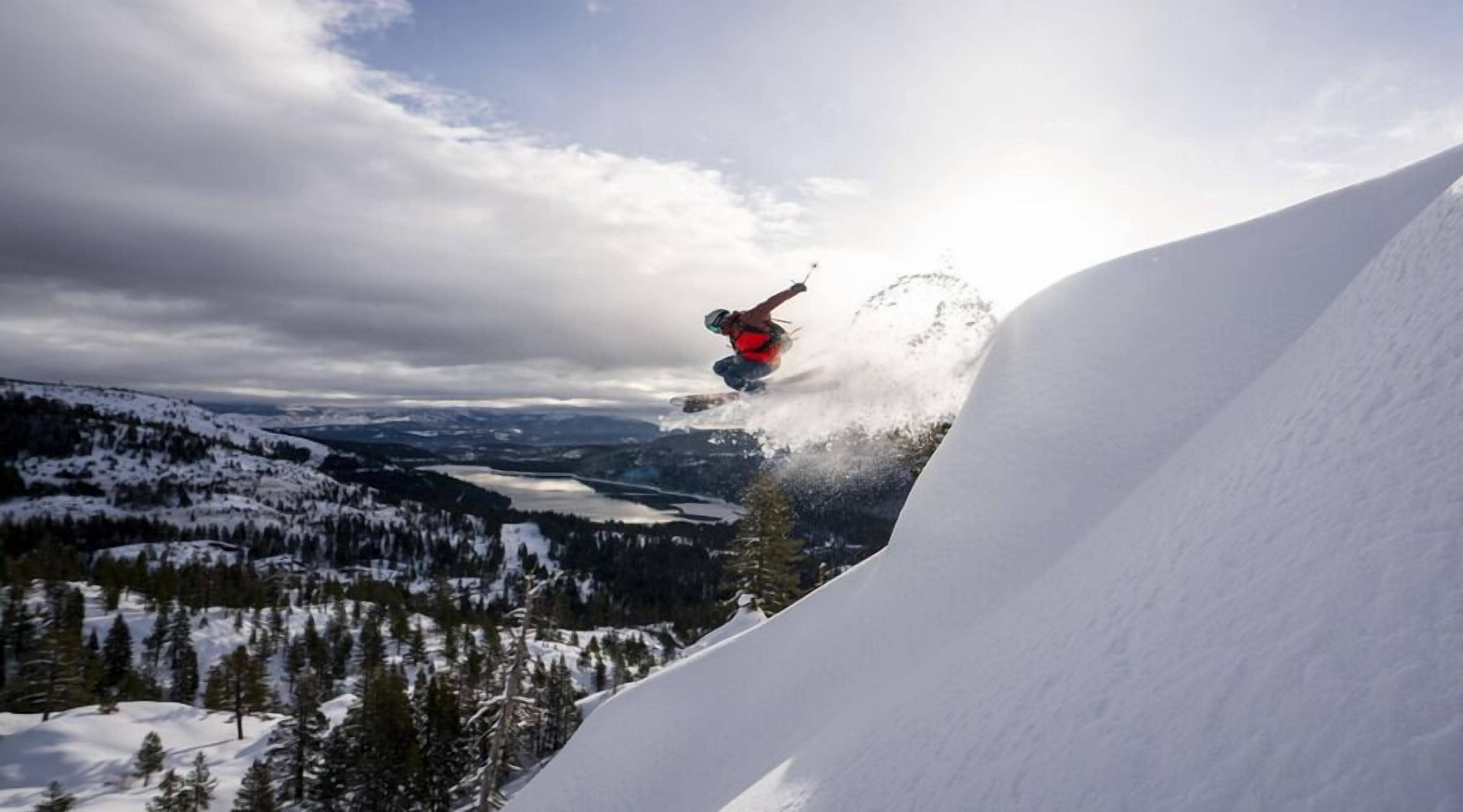 A snowboarder performing a jump over a snow-covered slope with a mountainous landscape in the background.
