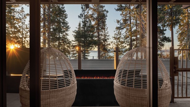 A view through a glass door with a fire feature and wicker hanging chairs. - evo Hotel Tahoe City (Tahoe City)
