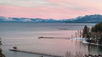 A lakeside view with a wooden pier extending into the water, surrounded by snow-covered mountains and a clear sky.