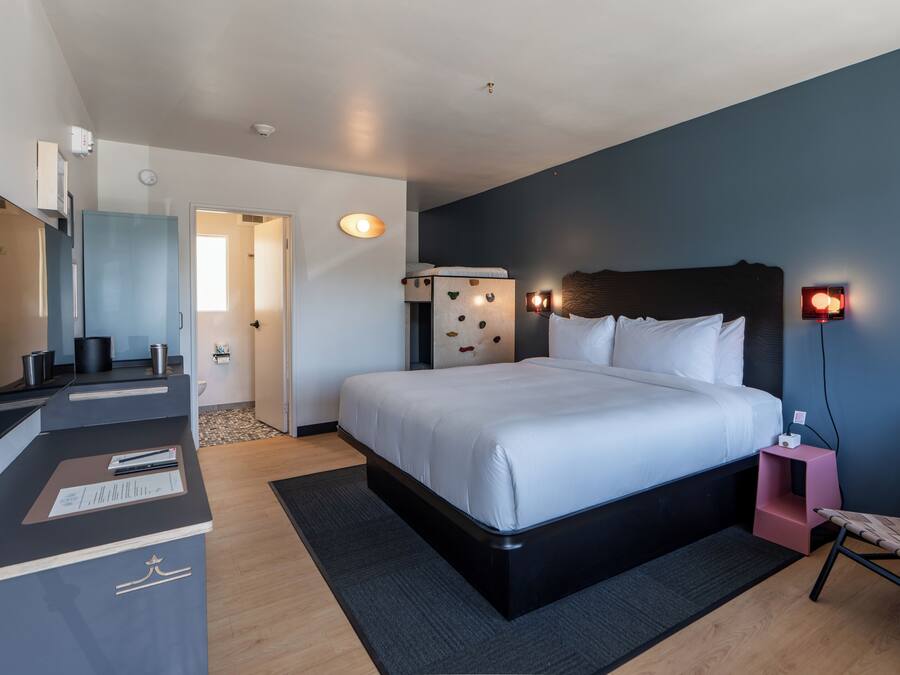 A modern hotel room with a large bed, a desk with a computer, a TV, and a small seating area.