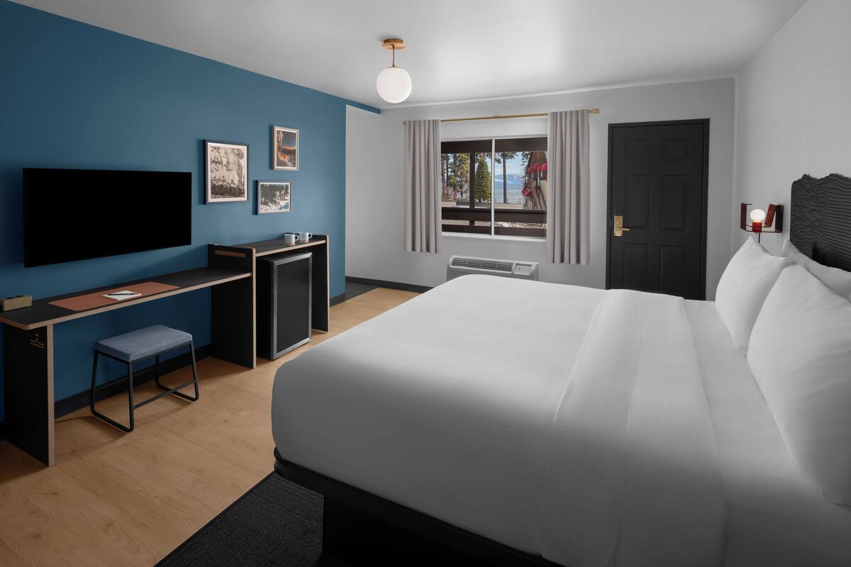 A modern hotel room with a large bed, a desk, a flat-screen TV, and a window with curtains.
