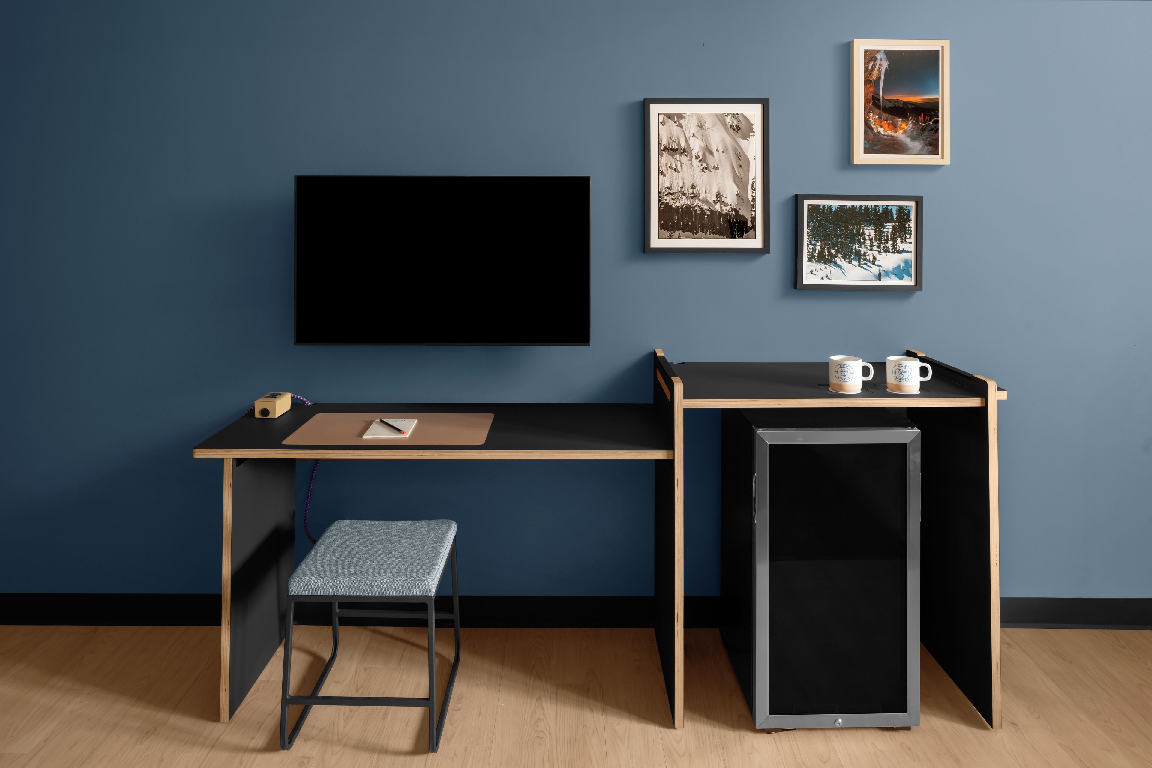 A modern room with a desk, a chair, a small cabinet, and a TV mounted on the wall.