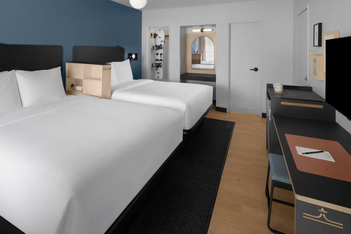 A hotel room with two beds, a desk, a TV, and a bathroom visible through an open door.