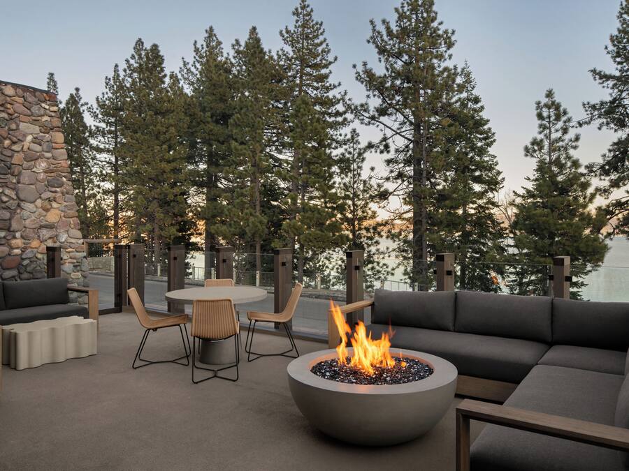 An outdoor seating area with a stone wall, a fire pit, and a view of trees.