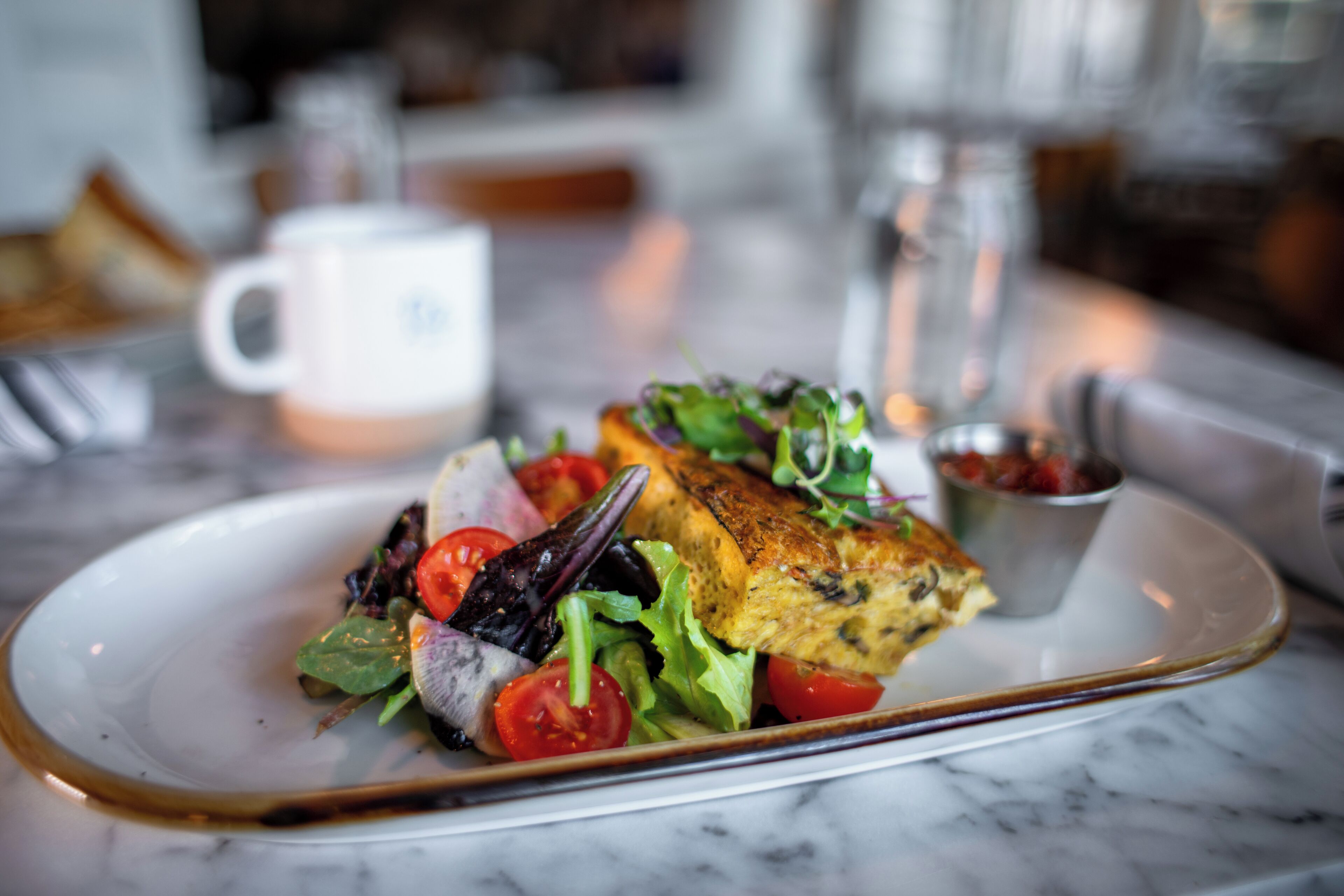 A plate with a grilled fish, salad, and a small bowl of sauce on a marble table.
