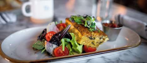 Un plato con pescado a la parrilla, ensalada y un recipiente pequeño con salsa sobre una mesa de mármol.
