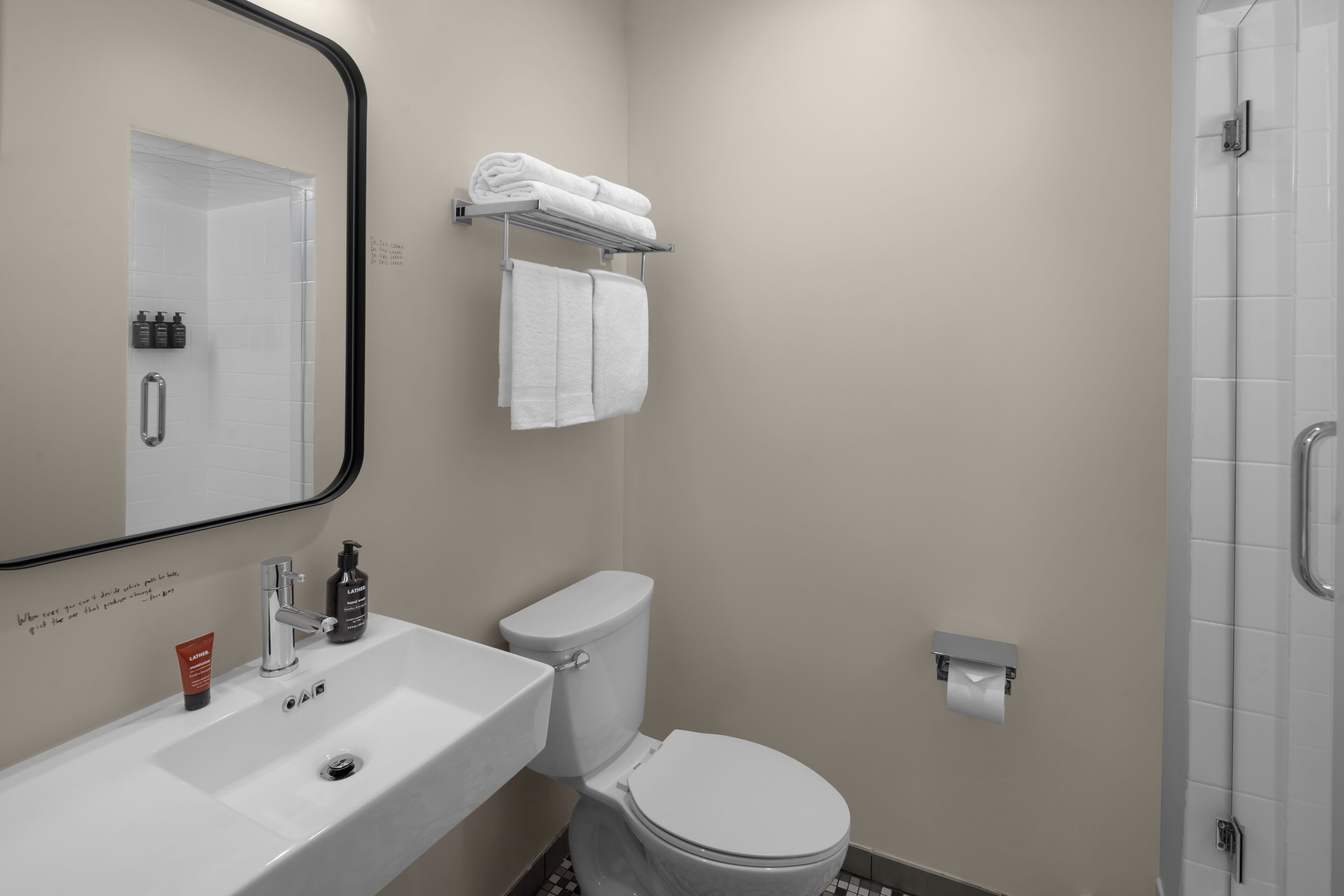 Baño con lavamanos blanco, inodoro, toallero con toallas, espejo y zona de ducha.