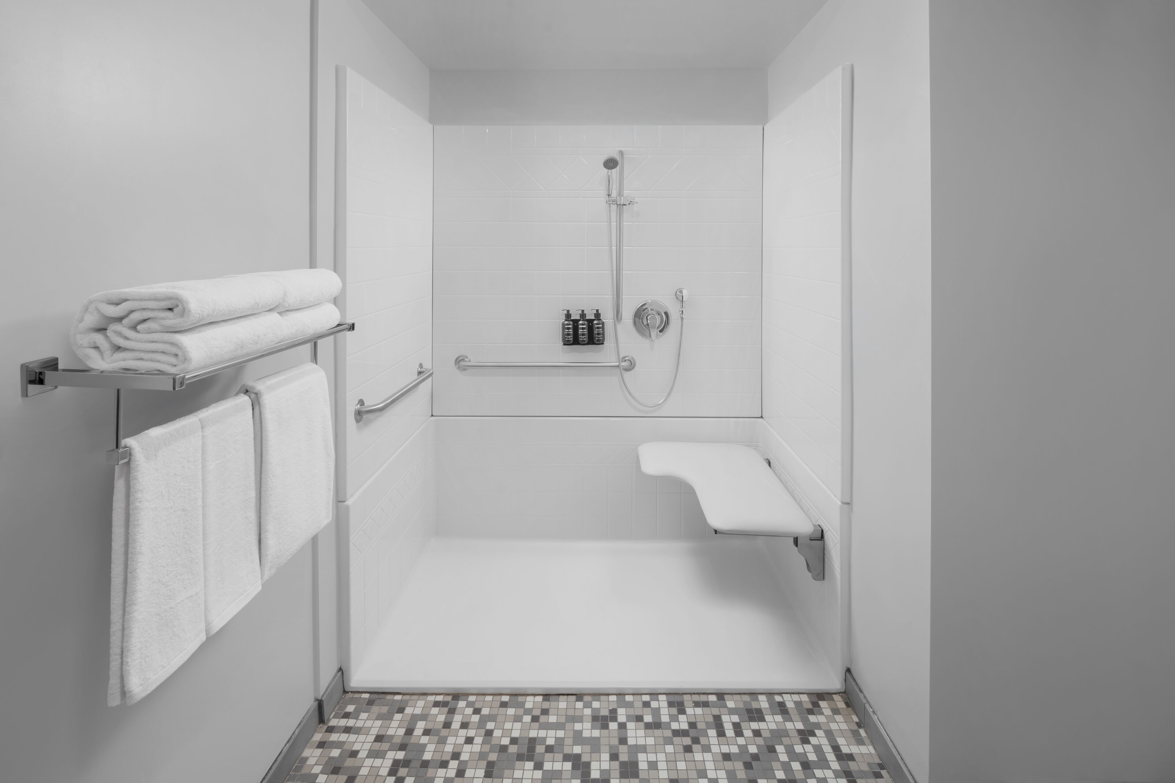 A modern bathroom with a shower, a towel rack, and a small shelf with toiletries.