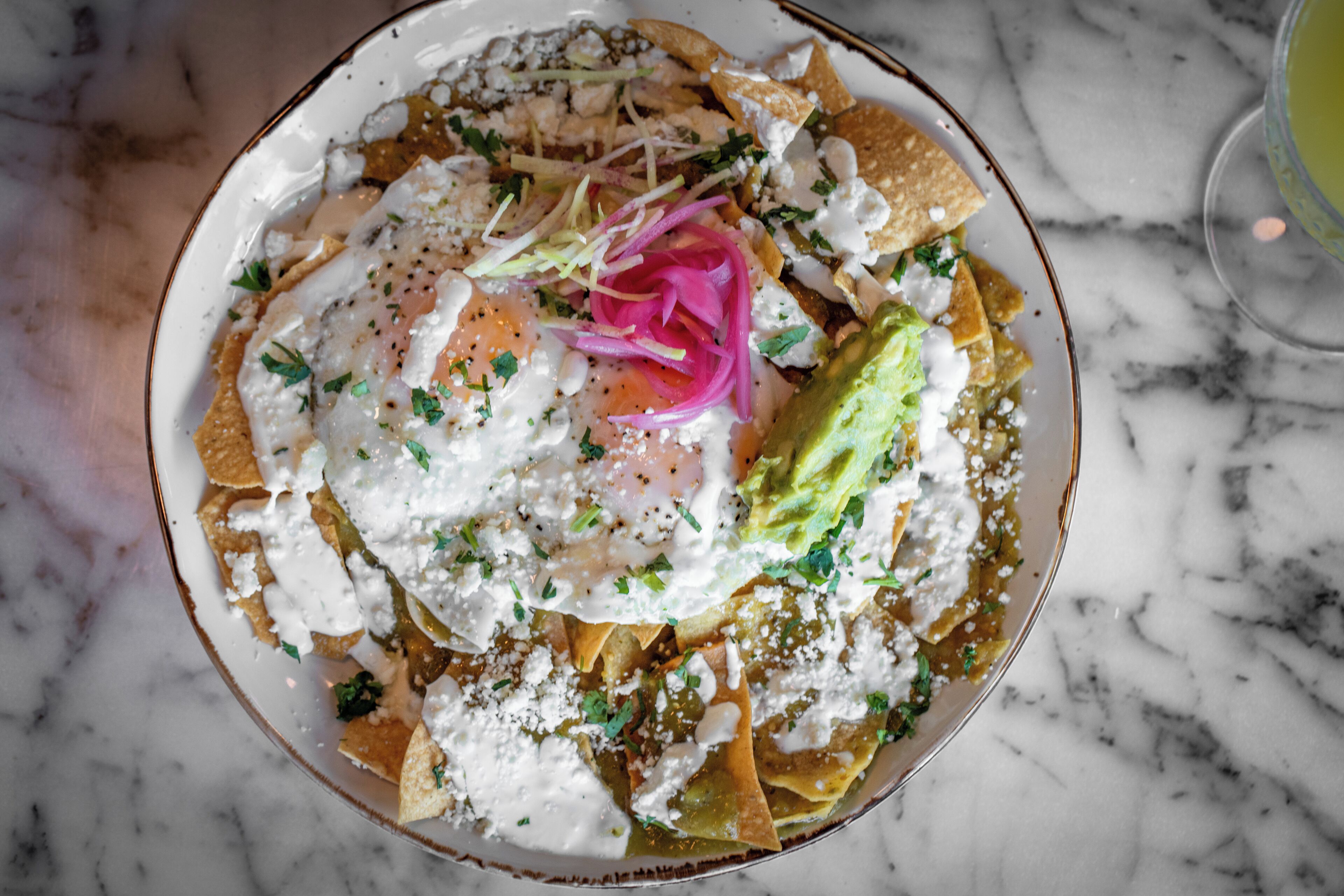 A plate of nachos topped with cheese, guacamole, and a fried egg, garnished with onions and herbs.