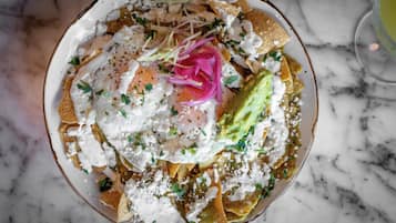 A plate of nachos topped with cheese, guacamole, and a fried egg, garnished with onions and herbs.