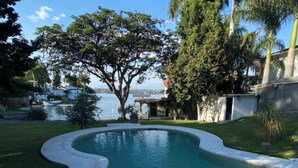 A swimming pool with a curved edge, surrounded by a well-maintained lawn and trees. - Room in House - Dream House on Lake Tequesquitengo (Jojutla)