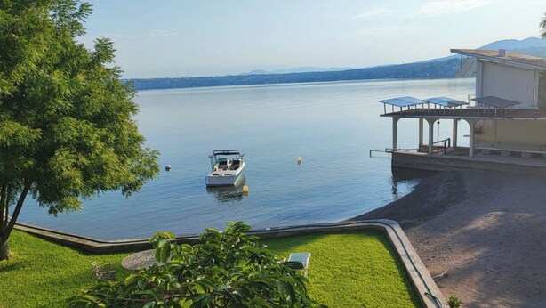 A boat on a calm lake with a house and a covered area on the right. - Room in House - Dream House on Lake Tequesquitengo (Jojutla)