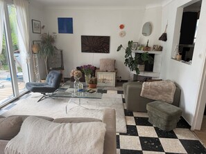 Un salon avec une table basse en verre, des canapés, une cheminée et une vue sur l’extérieur, accessible par une porte-fenêtre coulissante.