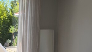 Une chambre avec un lit, un rideau blanc, une chaise blanche et une vue sur la verdure à l’extérieur.
