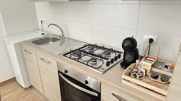 Cocina compacta con estufa a gas, horno y cafetera.