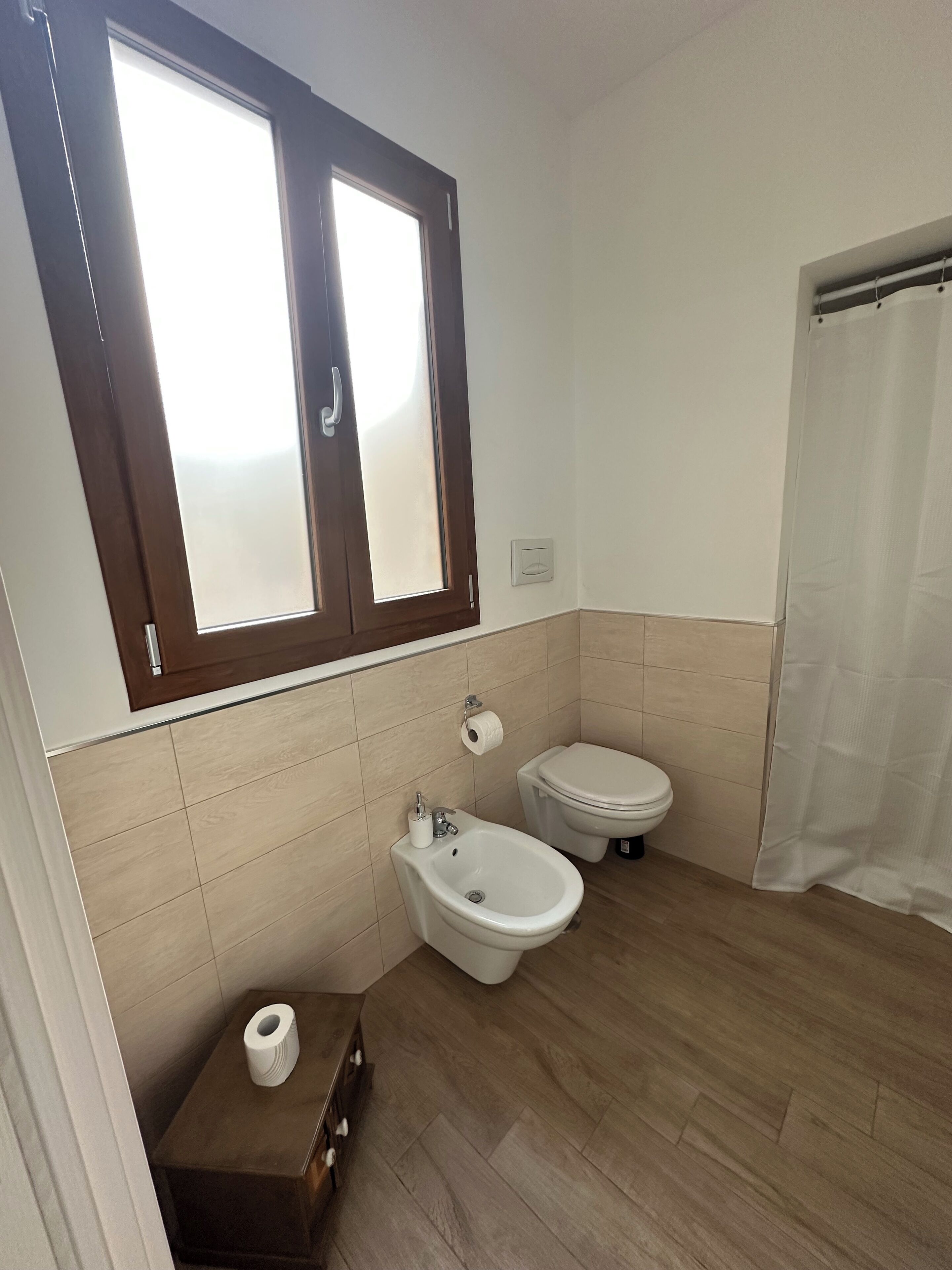 A bathroom with a toilet, bidet, and a window.