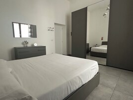 Un dormitorio moderno con cama, mesita de noche, espejo y armario.