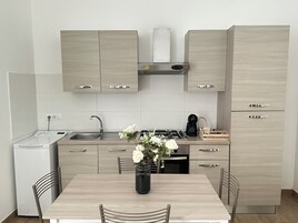 Una cocina moderna con armarios de madera clara, estufa integrada y un refrigerador pequeño.