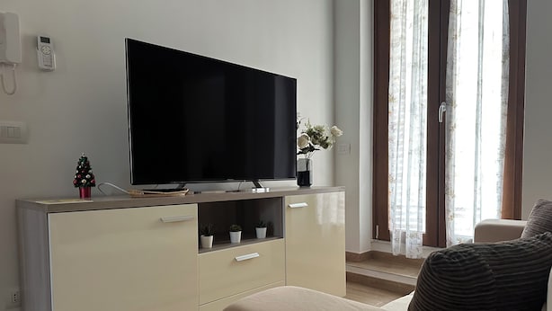A living room with a flat-screen TV on a wooden cabinet, a small Christmas tree, and a potted plant. - TOI Apartments (Brindisi)