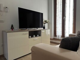 Una sala de estar con una televisión de pantalla plana sobre un mueble de madera, un pequeño árbol de Navidad y una planta en maceta.