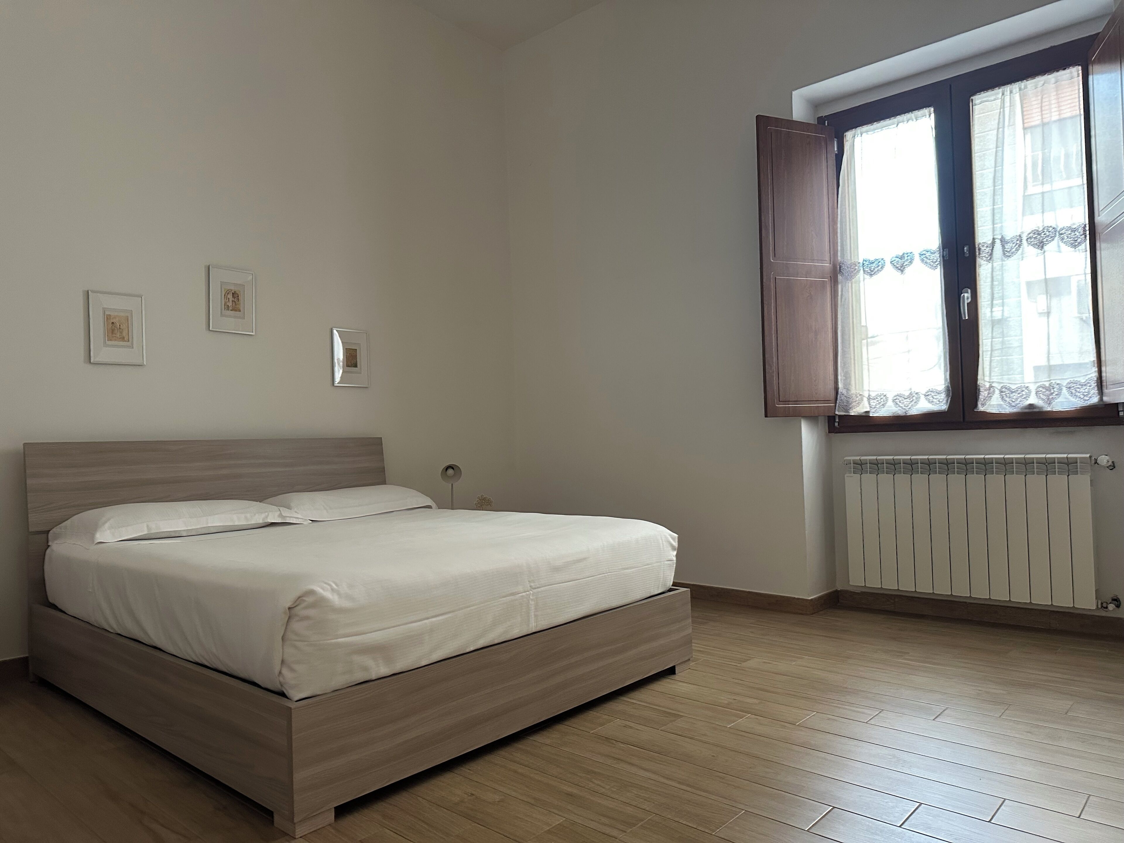 Un dormitorio con cama, ventana con cortinas y radiador.