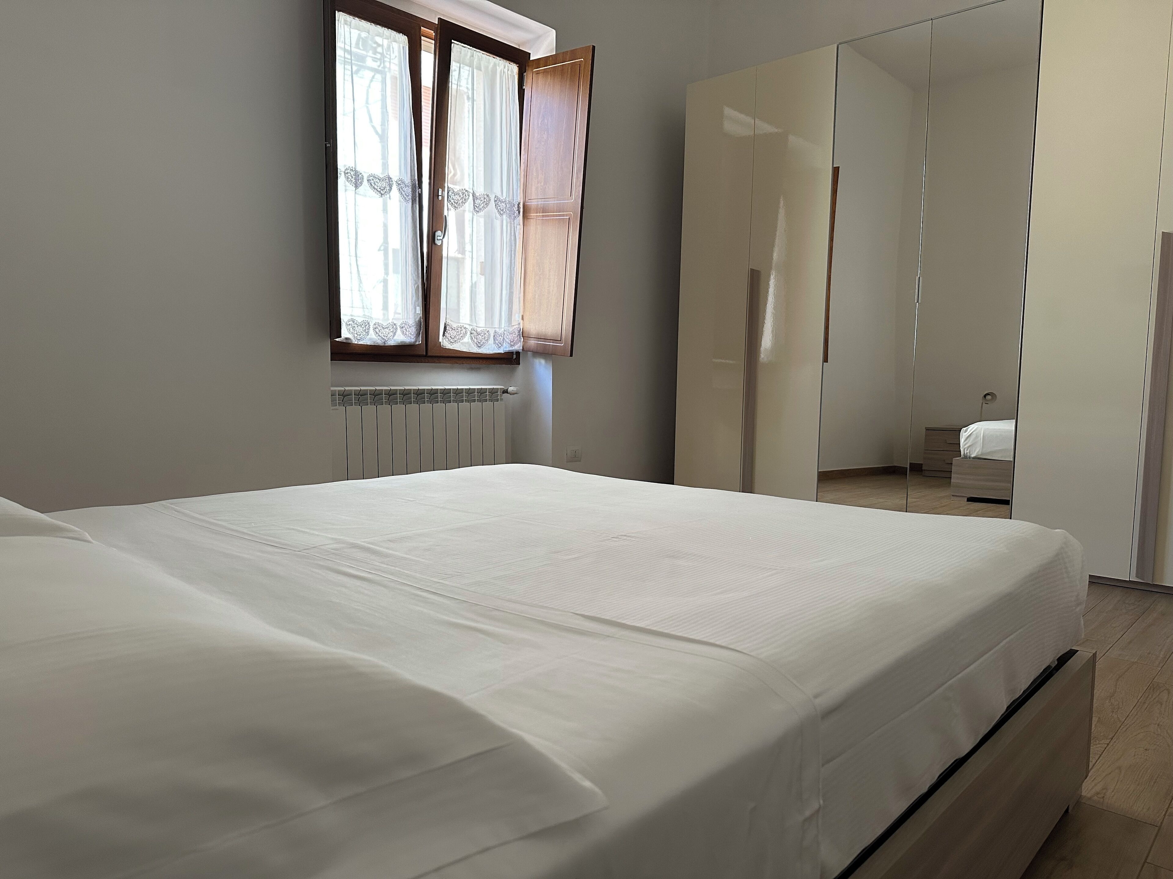 Une chambre à coucher avec un lit, un radiateur, une fenêtre avec des rideaux et une armoire avec un miroir.