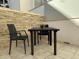 Un patio con pared de piedra, una mesa, dos sillas y una planta en maceta.