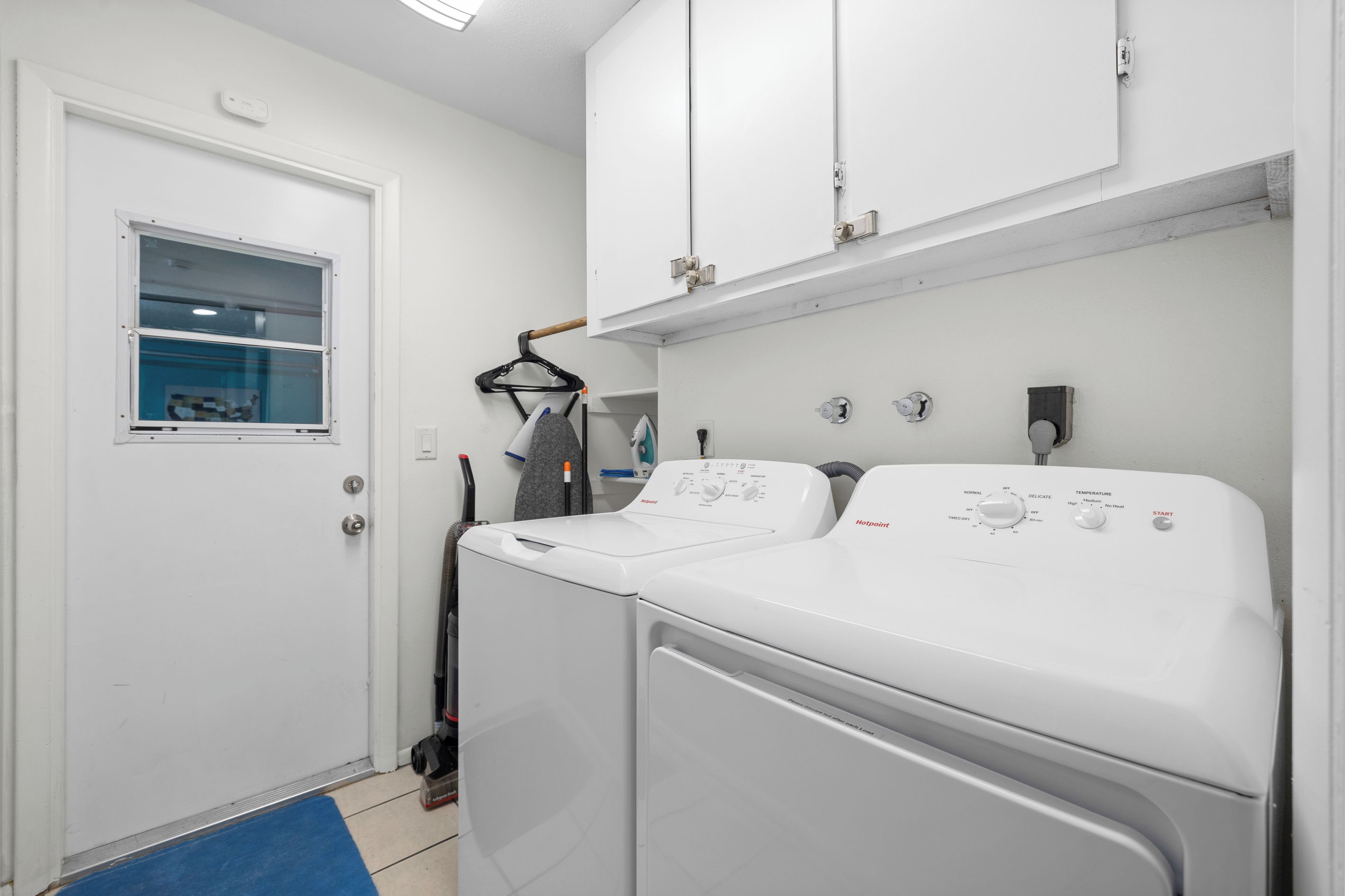 A laundry room with a front-loading washer and dryer, a window, and a door.
