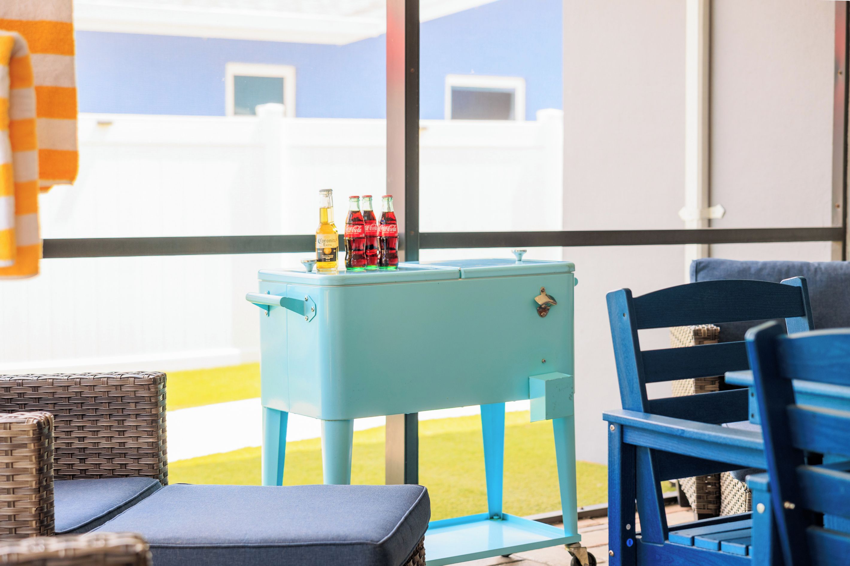 Ein Zimmer mit einem hellblauen Tisch, auf dem Flaschen stehen, ein Weidenstuhl und ein blauer Sessel.