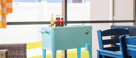 Ein Zimmer mit einem hellblauen Tisch, auf dem Flaschen stehen, ein Weidenstuhl und ein blauer Sessel.