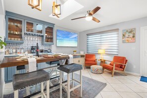 Una cocina moderna con taburetes de bar, ventilador de techo y un amplio ventanal con persianas.