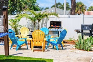 Un patio al aire libre con una parrilla, sillas y una hamaca.